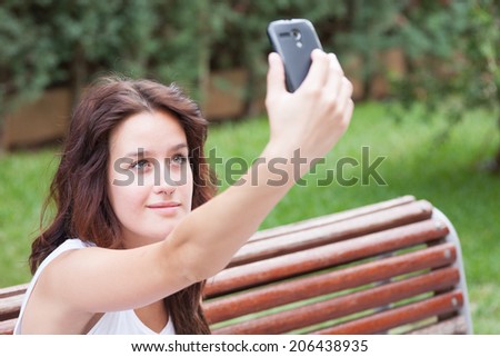 Green eyed girl makes a self-portrait with her smart phone. In the park.