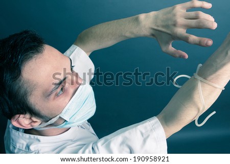 A doctor with a tourniquet in his right hand. Wearing a surgery mask and a medical gown