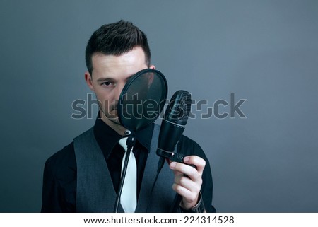 Guy covering his left eye with a microphone wearing a white tie