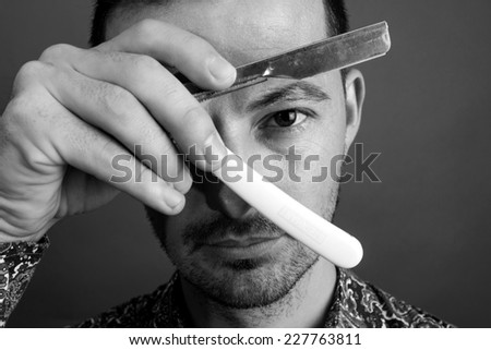 Closeup portrait of a men covering his left eye and looking through a shaving blade
