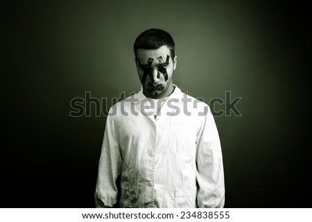 A crazy man dressed with a white gown having his eyes and his mouth covered with black duct tape.