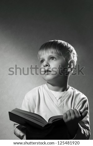 black and white portrait of cute little boy with book looking up