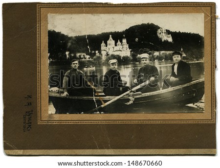 RUSSIAN EMPIRE - CIRCA 1910s:  Vintage photo of four man in the boat on the background of Svyatogorsk Monastery, Ukraine