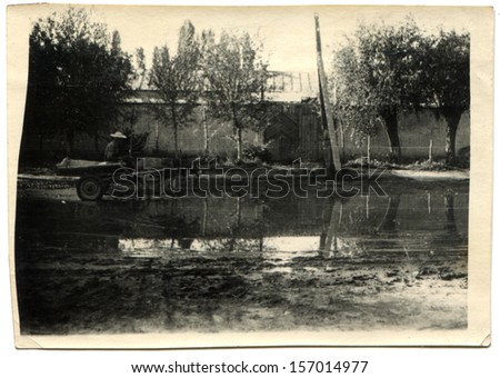 CHINA - CIRCA 1958: Chinese man in a straw hat crosses a large puddle on a donkey harnessed to a cart,  Chinese People\'s Republic, 1958