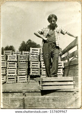 MAKHACHKALA, USSR - CIRCA 1950s: young man standing in the back of a truck next to a wooden box with fruit, Makhachkala, Dagestan, USSR, 1950s