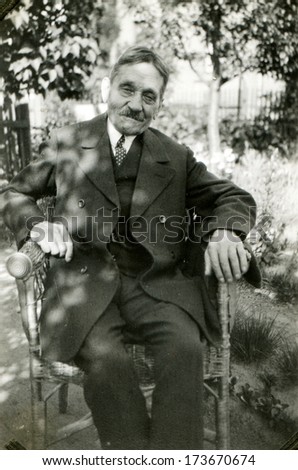 GERMANY - 1950s: An antique photo shows man in formal suit and tie seating in armchair in the garden
