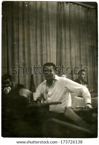 GERMANY - 1950s: An antique photo shows man seating at the dinner table on wich stay bouttle with wine