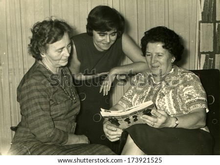 GERMANY - 1960s: An antique photo shows three women of different generations look fashion magazine