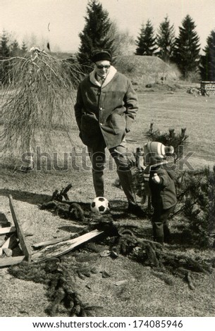 GERMANY -  1986: An antique photo shows man in a fur coat and hat with earflaps walks in the park with a small boy,