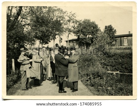 GERMANY -  1930s: An antique photo shows group of respectable men in raincoats and hats talking on the background of trees and single-story building