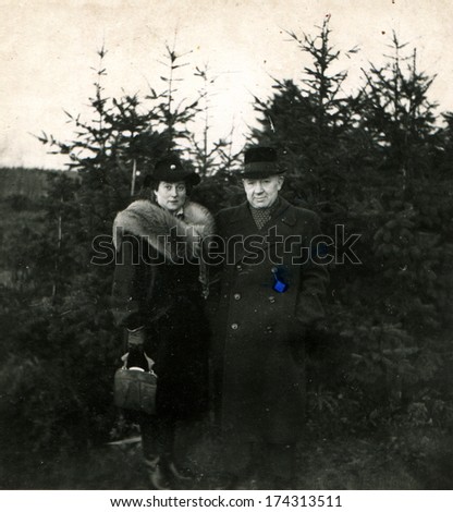 GERMANY -  CIRCA 1930s: An antique photo shows elderly couple on the background of fur trees