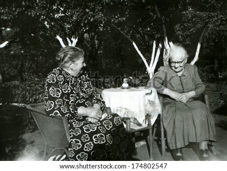 GERMANY -  CIRCA 1953: An antique photo shows two old women talking at the round table in the garden
