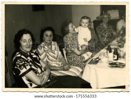GERMANY -  CIRCA 1960s: An antique photo shows group of elderly women sitting near the festive table, one of them holding a baby on her knees