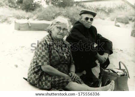 GERMANY, BERLIN -  CIRCA 1960s: An antique photo shows elderly couple sitting on the sand