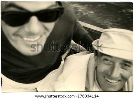 GERMANY - CIRCA 1960s: An antique photo of two smiling men, one of them wearing sunglasses, the second - in hat, looking at the camera from the bottom up