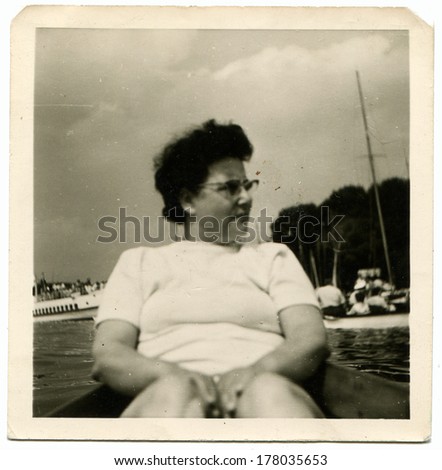 GERMANY -   May 15, 1969: An antique photo shows woman in glasses sits on the stern of the boat