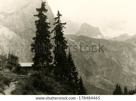 GERMANY - CIRCA August 8, 1968: An antique photo of Private house on the cliff beneath the tall pine trees on a background of mountain peaks