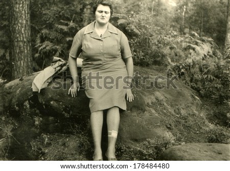 GERMANY, RANGSDORF - CIRCA 1950s: An antique photo of woman sitting on a moss-covered boulder in the woods on a background of ferns