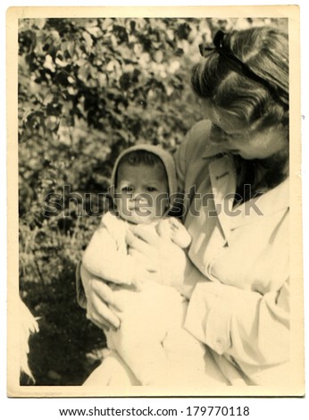GERMANY - CIRCA 1950s: An antique photo of woman in a garden holding a baby in her arms