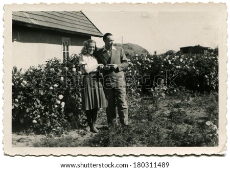 GERMANY - CIRCA 1950s: An antique photo of man and woman posing against the backdrop of a private house and a flower garden
