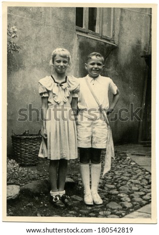 GERMANY - CIRCA 1930s: An antique photo of girl and boy in white dresses on the background of house
