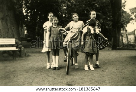 GERMANY, TONNING - CIRCA 1930s: An antique photo of five girls posing in the park, one of them sitting on a bicycle, Tonning