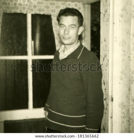 GERMANY - CIRCA 1930s: An antique photo of middle-aged man in a white shirt and jersey posing in a room against the window