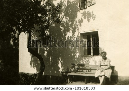 GERMANY - CIRCA 1940s: An antique photo of middle-aged woman posing on a bench under the window of an apartment building