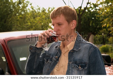 Young men in jeans jacket with glass of red wine in the garden