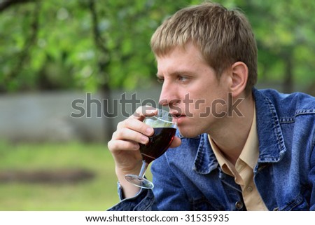 Young men in jeans jacket with glass of red wine in the garden