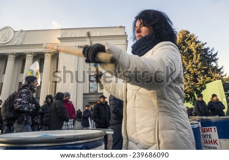 KIEV, UKRAINE - December 23, 2014: Woman protesting drumming on metal barrel on the background of the Verkhovna Rada. -- To break through the cordon of police and four special forces in full uniform