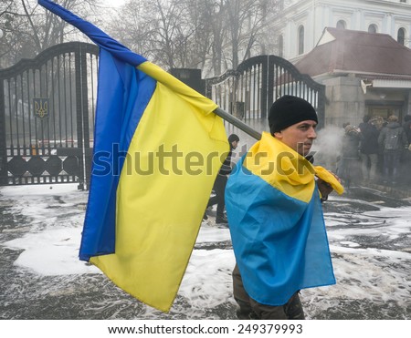 KIEV, UKRAINE - February 2, 2015: Soldier battalion Aydar with the national flag on his shoulders holding a Ukrainian flag on background extinguished tires near Ministry of Defense of Ukraine in Kiev