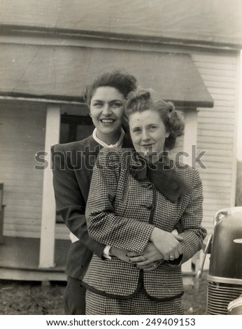 CANADA - CIRCA 1950s: Reproduction of an antique photo shows two women in business suits posing against private home near a car