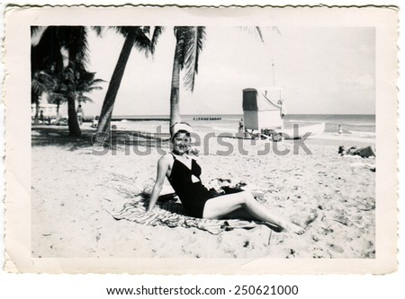 HAITI - CIRCA 1950s: Reproduction of an antique photo shows woman in swimsuit posing on the beach against the backdrop of palm trees and ocean