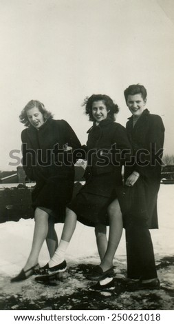 CANADA - CIRCA 1950s: Reproduction of an antique photo shows two girls and a boy show his feet, standing on a background snowy lawn. Everyone laughs.