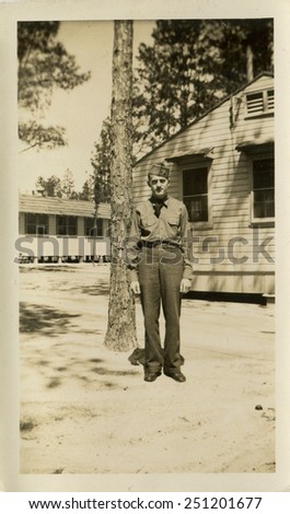 CANADA - CIRCA 1940s: Reproduction of an antique photo shows man in military uniform posing against the backdrop of one-story buildings, obviously barracks