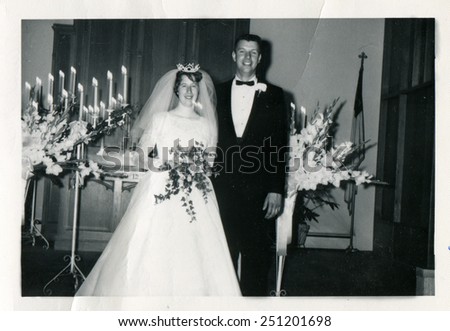 CANADA - CIRCA 1950s: Reproduction of an antique photo shows Bride and groom posing in the church, the bride holding a bouquet, on a candlestick burning candles