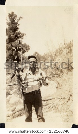 CANADA - CIRCA 1940s: Reproduction of an antique photo shows hunter with a gun killed roe deer on his shoulders posing on a forest background