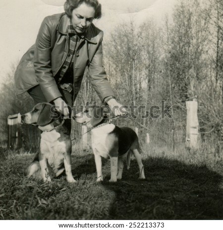 CANADA - CIRCA 1940s: Reproduction of an antique photo shows woman in leather jacket on a walk bent over two hunting dogs on leashes