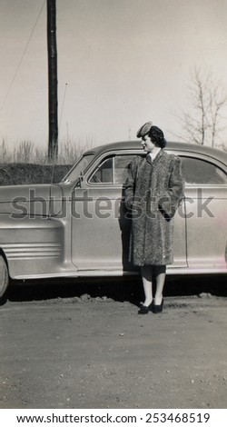 CANADA - CIRCA 1940s: Reproduction of an antique photo shows young woman in a fur coat and astrakhan hat posing near a luxury car
