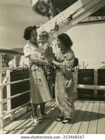 CANADA - CIRCA 1950s: Reproduction of an antique photo shows Two Japanese women on the deck of the ship, one of them holding a Caucasian boy, the other wearing a kimono, both laughing