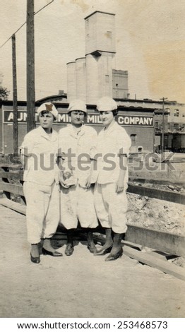 CANADA - CIRCA 1940s: Reproduction of an antique photo shows Three young women in white working suits posing against the backdrop of the mill