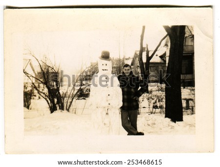 CANADA - CIRCA 1940s: Reproduction of an antique photo shows man posing next to a snowman on the background of the snow-covered streets