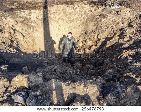 NIKISINO, UKRAINE - Feb 27, 2015: A man stands in a giant funnel height of more than two human growth. Village Nikishino located 20 km from Debaltseve, Ukrainian military was abandoned three days ago.