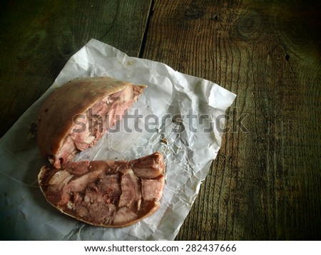 Homemade headcheese sheathed pig stomach on a piece of oiled packing paper on raw wooden background. Grunge style.