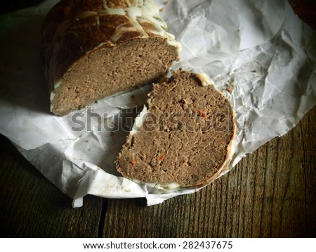 Homemade goose pate in a natural casing on a piece of oiled packing paper on raw wooden background. Grunge style.