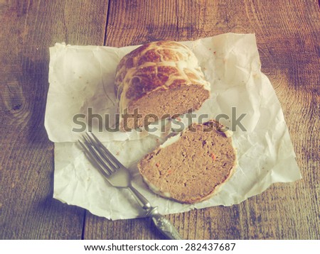 Homemade goose pate in a natural casing on a piece of oiled packing paper on raw wooden background. Grunge style.