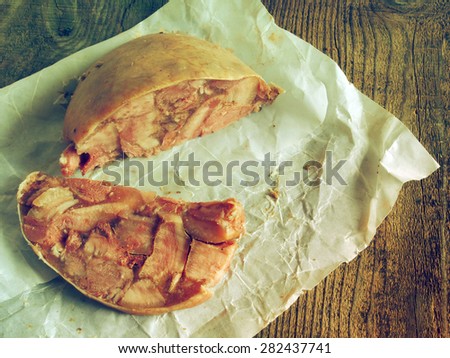 Homemade headcheese sheathed pig stomach on a piece of oiled packing paper on raw wooden background. Grunge style.