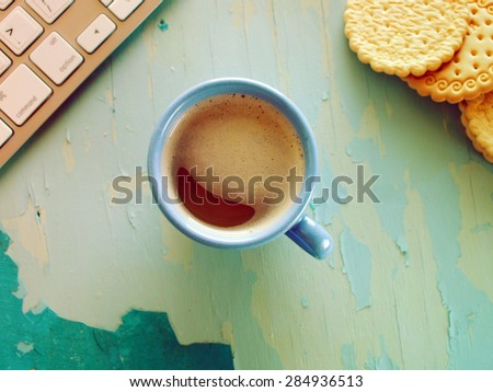 Computer keyboard, cup of coffee and biscuits on blue painted weathering table. Grunge style