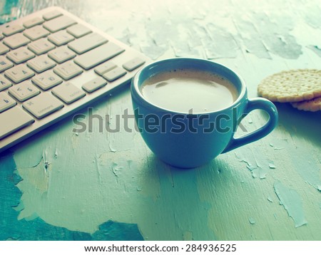 Computer keyboard, cup of coffee and biscuits on blue painted weathering table. Grunge style